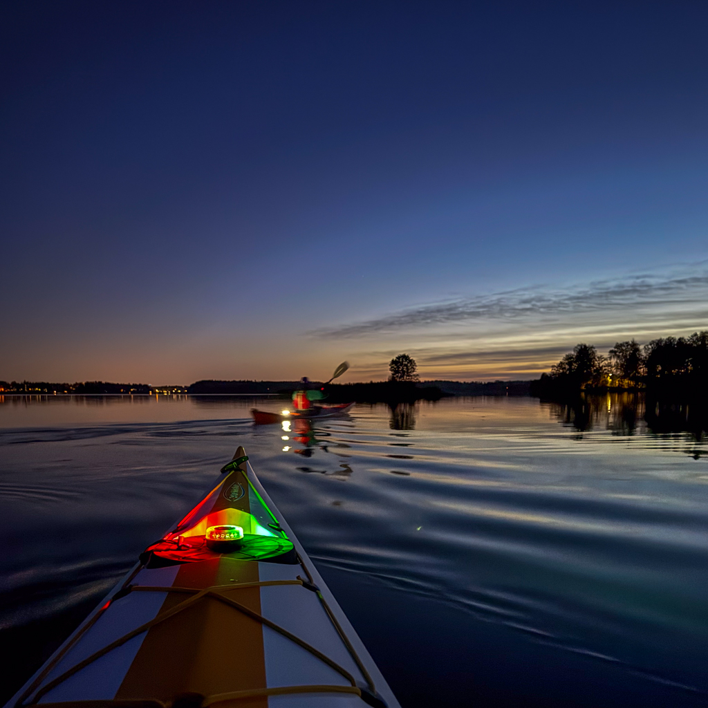 Kajakin keula punaisine ja vihreine valoineen tyynellä järvellä auringonlaskun jälkeen.